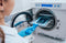 A medical worker wearing blue latex gloves inserts a tray of covered medical instruments inside an autoclave.