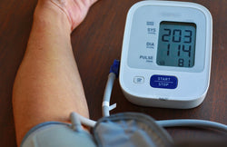 A person checks blood pressure at home using a blue and white digital monitor, revealing high test results.