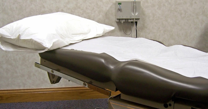 A doctor’s office medical exam table sits ready for use in a clean, well-lit medical room.