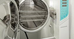 A new medical autoclave with a blue operating panel is open, revealing three large, empty sterilization shelves inside.