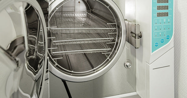 A new medical autoclave with a blue operating panel is open, revealing three large, empty sterilization shelves inside.