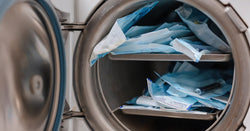 A small autoclave sterilizes medical instruments sealed in blue pouches, which are stacked to capacity.