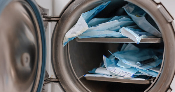 A small autoclave sterilizes medical instruments sealed in blue pouches, which are stacked to capacity.