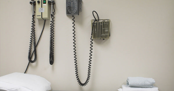 An exam table with a clean sheet and pillow, along with a neatly folded gown on top, and medical equipment on the wall above.