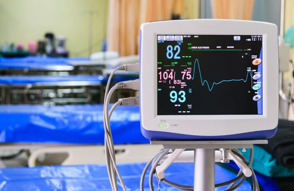 A vital signs monitor in a medical setting displays a patient's blood pressure, heart rate, and oxygen level.