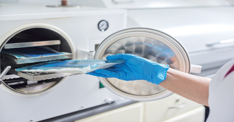 A healthcare worker loads medical instruments into an autoclave for medical equipment sterilization in a clinical setting.