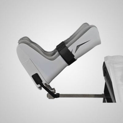 G Stirrups leg positioning device attached to an examination table, showing the adjustable strap and angled positioning for patient support during medical procedures.